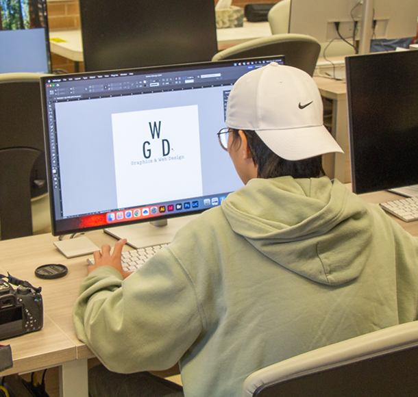A photo of a graphic design student working on their assignment in the computer lab on campus. 
